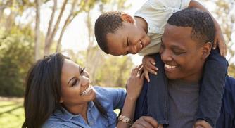 An image of a child on top of his father's shoulders while his mother stands next to them both while smiling